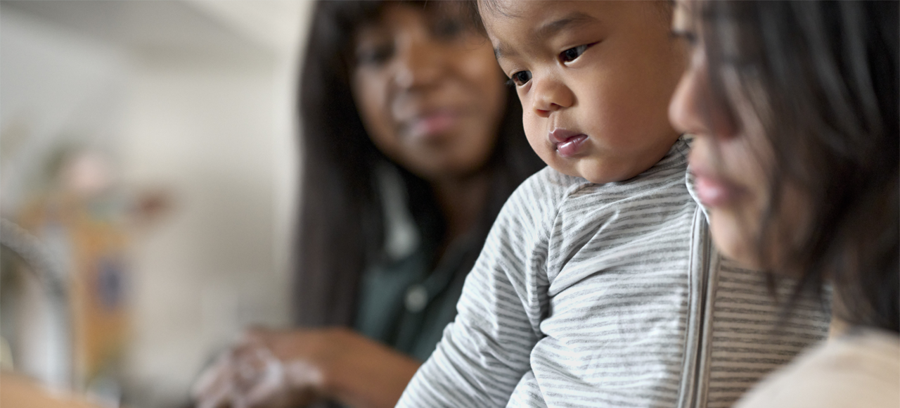 A pediatrician seated with a family — a mother smiling as her baby looks on