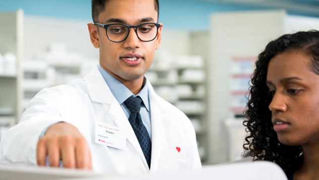 A CVS pharmacist with a red heart on his coat advising a customer at the counter