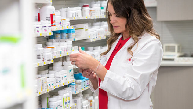A CVS pharmacist in a white coat checking medication on a stocked shelf